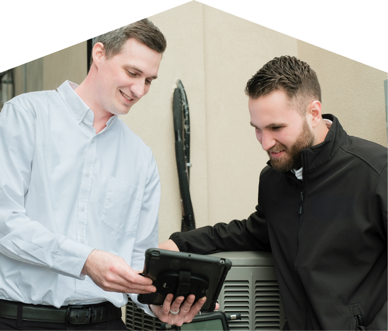 A 669 Heat technician in a white shirt shows service details on a tablet to a smiling client in a black jacket, standing beside an AC unit outside a beige building. A 669 Heat technician in a white shirt shows service details on a tablet to a smiling client in a black jacket, standing beside an AC unit outside a beige building.