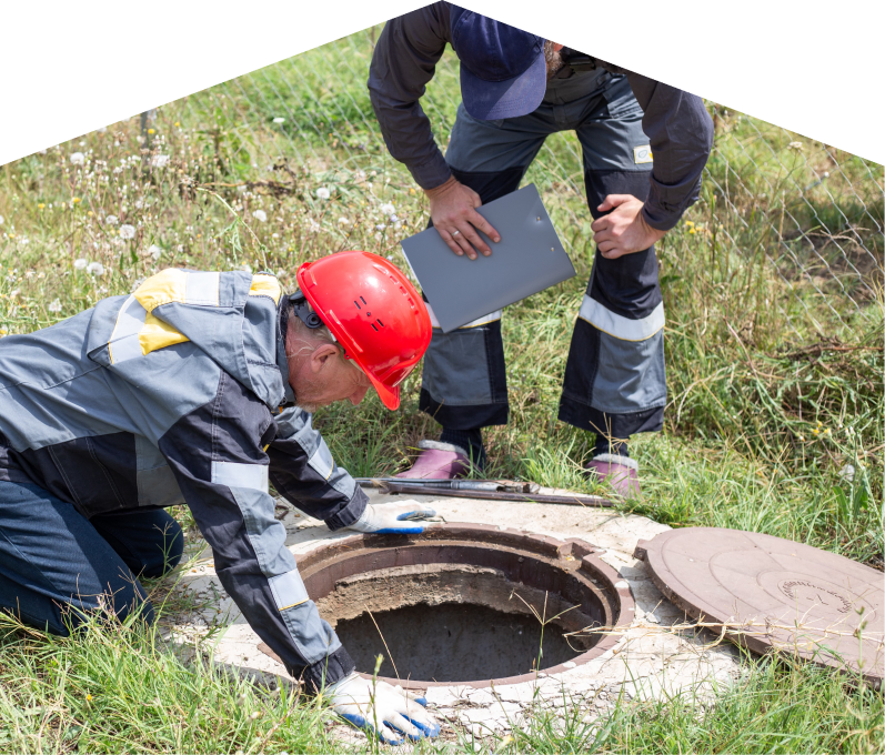 669 Heat sewer crew inspecting an open manhole in a grassy field, with one member documenting findings on a clipboard. 669 Heat sewer crew inspecting an open manhole in a grassy field, with one member documenting findings on a clipboard.