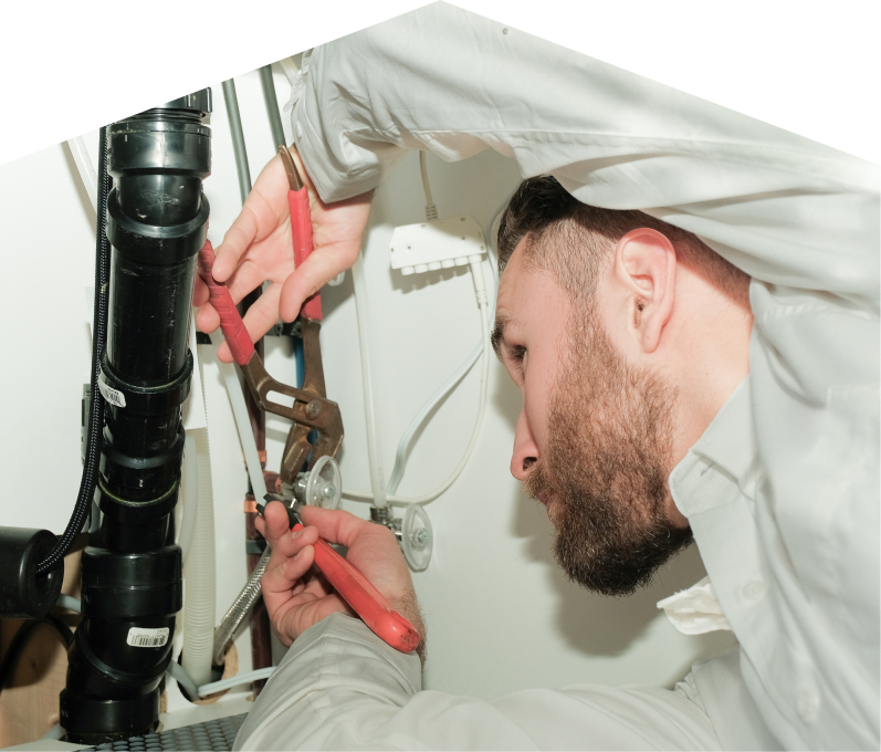 669 Heat plumbing specialist uses hand tools to tighten pipe fittings beneath a sink during a repair, with visible wiring and drainage lines in the background. 669 Heat plumbing specialist uses hand tools to tighten pipe fittings beneath a sink during a repair, with visible wiring and drainage lines in the background.