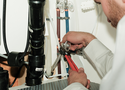 Using two pipe wrenches, a 669 Heat professional plumber services a pipe connection near a vertical flue or vent pipe. Using two pipe wrenches, a 669 Heat professional plumber services a pipe connection near a vertical flue or vent pipe.